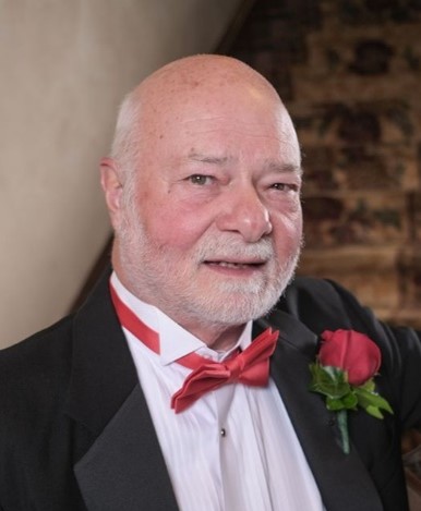 Jack Pace, a man with grey hair, beard, and mustache, wearing a dinner suit with a red bowtie and rose
